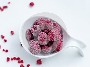 Close up of frozen rasberries in a white bowl on a white background with selective focus. Top view