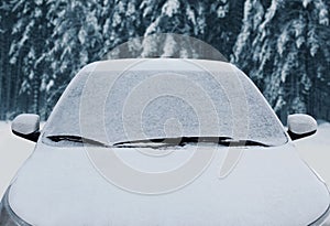 Close up frozen winter car covered snow, view front window windshield and hood on snowy forest