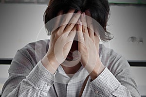 Close up frustrated stressed young Asian business man with hands covering face and feeling disappointed or exhausted with job.