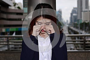 Close up frustrated stressed young Asian businesswoman crying closed face with her hands at outside office.