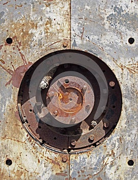 close up full frame detail of old rusting machinery with circular hole in steel plates with bolts and round drive shaft in the