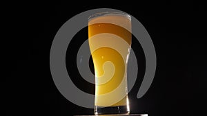 Close-up of a full glass of beer with foam spinning on a black background.