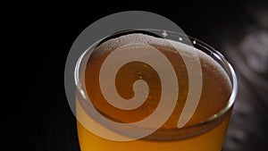 Close-up of a full glass of beer spinning on a wooden background in the dark.