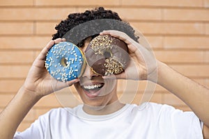 Close-up of a funny African-American man making face and eyes out of chocolate and blue donuts