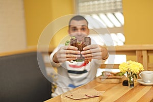 Close up funny blurred protrait of young man hold bitten sandwich by his two hands. Sandwich in focus. light background.