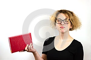 Close-up of a funny girl student with glasses and a strange hairstyle, a mess on her head, holding a book in her hands