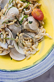 Close up Fusilli Avellinesi pasta with clams and tomato in yellow and blue plate