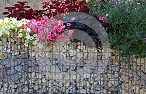 Close-up of a gabion support wall with wire mesh reinforcement topped with pebbles and tiles