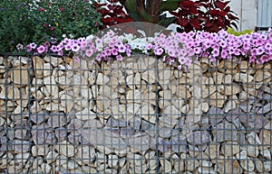 Close-up of a gabion support wall with wire mesh reinforcement topped with pebbles and tiles