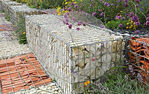 Close-up of a gabion support wall with wire mesh reinforcement topped with pebbles and tiles