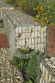 Close-up of a gabion support wall with wire mesh reinforcement topped with pebbles and tiles