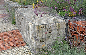 Close-up of a gabion support wall with wire mesh reinforcement topped with pebbles and tiles