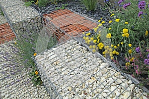 Close-up of a gabion support wall with wire mesh reinforcement topped with pebbles and tiles