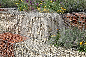 Close-up of a gabion support wall with wire mesh reinforcement topped with pebbles and tiles