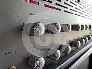 Close-up the gain silver knob of the boutique distortion guitar amplifier with blurred gray control panel and  knob with red LED