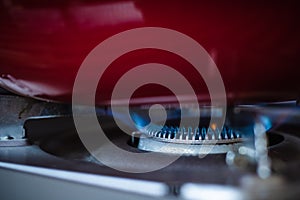 Close up gas stove with blue flames of burning gas with red pan