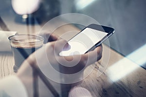 Close up of generic design smart phone holding in female hands for texting message. Cup coffee on the table