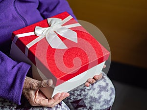 Close-up of a gift box in the hands of a senior woman. Concept of aged people and holiday