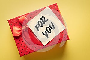 Close-up of a gift box with a note with the words for you on a yellow background: expression of gratitude or love