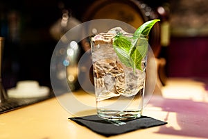Close up of gin tonic glass inside bar on top of bar counter with ice cubes and basil leaves at night photo