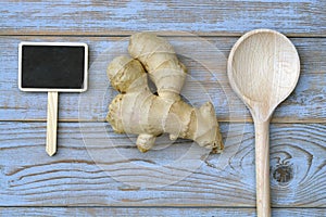 Close up of ginger root on old wooden planks background with wooden spoon and blackboard tag with empty copy space