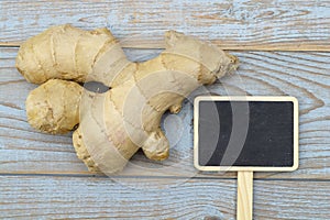 Close up of ginger root on old wooden planks background with wooden spoon and blackboard tag with empty copy space