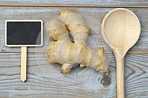 Close up of ginger root on a old wooden planks background with wooden spoon and blackboard tag with empty copy space