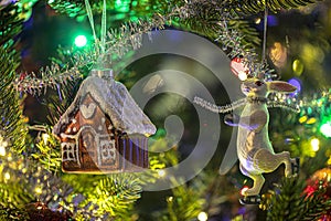 Close up of gingerbread toy houses, rabbit and a christms tree decoration hanging on a fir branch