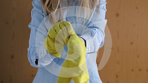 Close-up, of a girl in a blue, shirt putting yellow rubber, gloves on her hands.