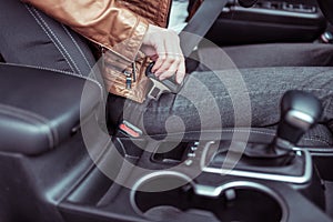 Close-up of girl in car interior fastens her seat belt. Winter and autumn in city. Car interior, automatic transmission