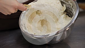 Close-up of a girl cook mixing dough with a silicone spatula in a metal bowl.