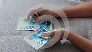 Close up of a girl counting Israeli money. Counting 200 Israeli shekel bills - close up on large amount of money.