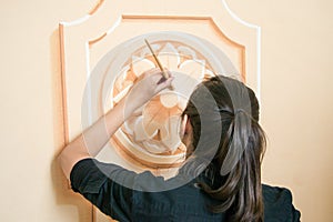 Close up of a girl (dark hair and black clothes) decorating a wall with a floral motive element with a brush