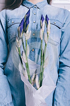 Close-up of a girl in a denim shirt holding a bouquet of unblown flowers iris