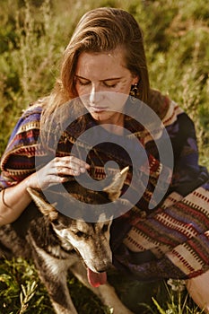 close-up. Girl in ethno cape with natural beauty without makeup strokes the dog& x27;s hand sitting in the grass