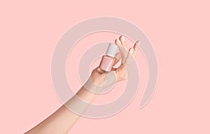 Close up of girl hands holding bottle of nail enamel on pink background, panorama