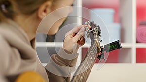 Close-up girl hands tuning guitar. Young woman checking pegs of acoustic guitar.