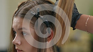 Close-up of a girl head with hairclips in her hair. A hand in a black rubber glove removes the hairclip.