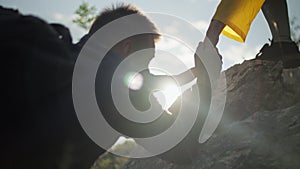 Close-up of a girl helping a boy climb a rock.