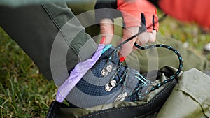 Close-up of a girl hiker& x27;s hand in red gloves and red manicure tying the laces on her boots. The concept of mountain