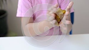 Close-up of a girl hold and stretching yellow with golden glitter slime at a white table. child playing with a slime toy. Making s