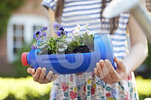 Close Up Of Girl Holding Recycled Plant Holder From Plastic Bottle Packaging Waste In Garden At Home