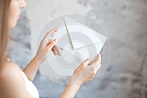 Close-up girl holds with two hands a white envelope wedding invitation notice on a gray background