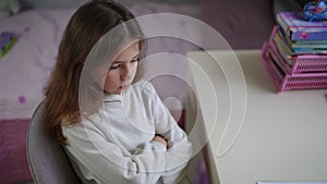 Close-up. A girl in home clothes sits on a chair, arms crossed over her chest, and looks at the table, on which lies an