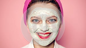 Close-up of a girl with a mask on her face with a wide-open eyes smiling. Funny girl with cosmetic mask on her face