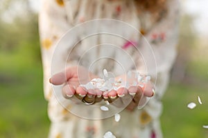 A close-up of a girl palm blows off a handful of white petals that fell from a flowering tree. Attractive young girl with flowers