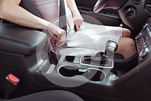 Close-up, a girl in pink dress in car interior fastens her seat belt, interior of car automatic gearbox, armrest, safety