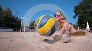 CLOSE UP: Girl playing volleyball jumps into sand and strikes ball with hand.