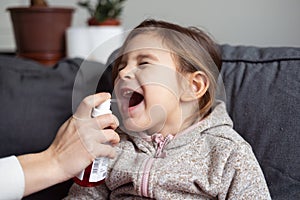 Close up of girl portrait and mother hand with spray for throat. Kids flu medical treatment concept photo