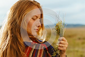 close-up girl in profile with red hair holds in her hand a bouquet of herbs and looks at it